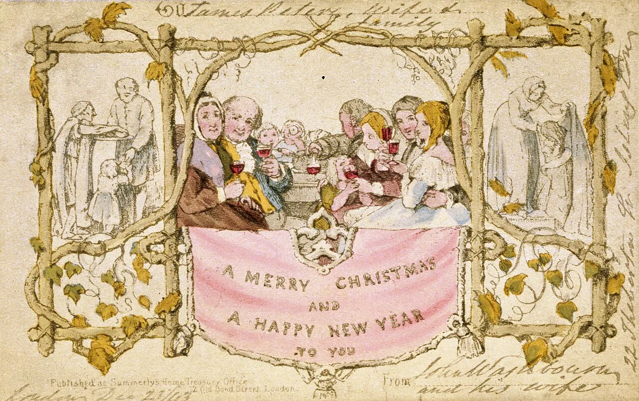 The first Christmas card: a family at a table raising glasses, framed by twigs, with a pink banner that reads A Merry Christmas and a Happy New Year to You.