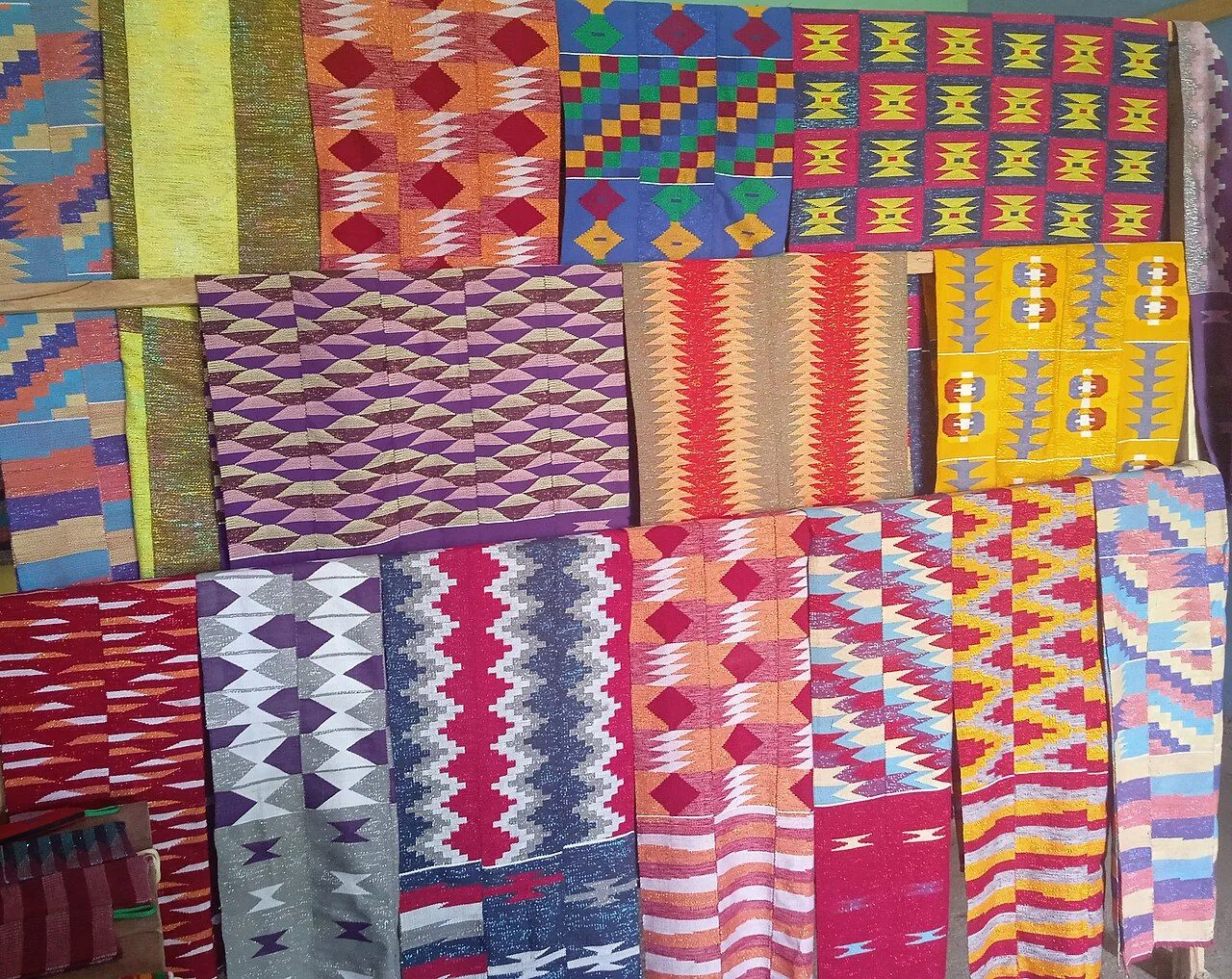 Rows of hand-woven cloth in bright stripes and diamond patterns hang on a rail.